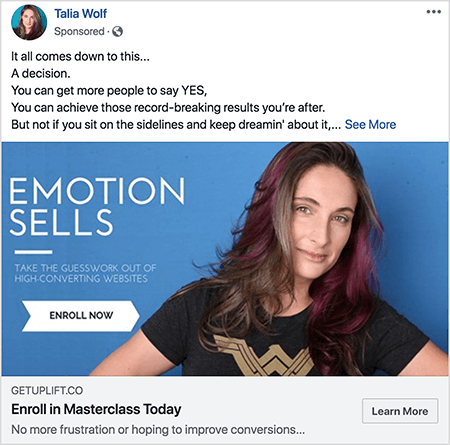 Това е екранна снимка на реклама във Facebook за майсторски клас от Talia Wolf. В рекламния текст всяко изречение е на отделен ред. Пише „Всичко се свежда до това... Решение. Можете да накарате повече хора да кажат ДА. Можете да постигнете тези рекордни резултати, които търсите. Но не и ако седите отстрани и продължавате да мечтаете за това... „След този текст е връзката Вижте още. Рекламното изображение има син фон с бял текст и снимка на Талия от гърдите нагоре. Тя е бяла жена с кафява и лилава коса, която пада под раменете. Тя е облечена в черна тениска със златно лого на Wonder Woman. Текстът вляво от нейната снимка казва „Emotion Sells“ и „Извадете предположенията от високо конвертиращите уебсайтове“. Под този текст има бяла стрелка с черен текст, която казва „Запишете се сега“. Под изображението е следното заглавие и текст: „Getuplift.co“ и „Запишете се в Masterclass Today“ и „Няма повече разочарование или надежда за подобряване на реализациите“. Бутон Научете повече се появява в долния десен ъгъл.